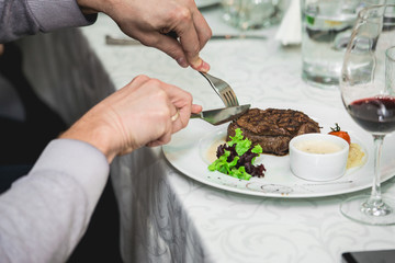 fresh grilled bbq roast beef steak and sauce on a white plate with green leaf of salad. soup sauce small jug glass served on a table in a restaurant
