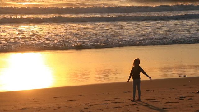 Small girl meditating on beach at sunset