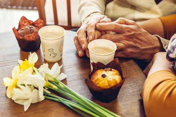 Senior couple holds hands in the cafe drinking coffee. Celebrating anniversary.