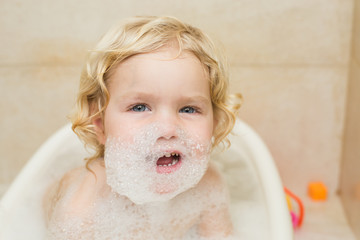 smiling child bathing in the bathroom with foam