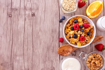 Cereal and ingredients for a healthy breakfast forming a side border over a wood background. Top...