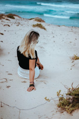 Woman sitting in white sand dune landscape on the Atlantic coastline. Waves hitting coast in background. Sao Vicente Cape Verde