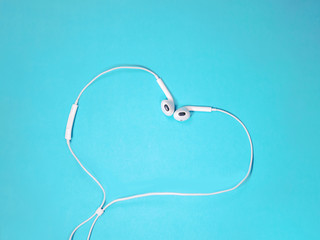 white earphones heart shaped on a blue background. Music concept. Copy space