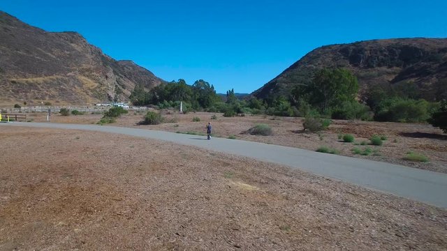 Aerial footage following a man riding an electric unicycle down a road in California.