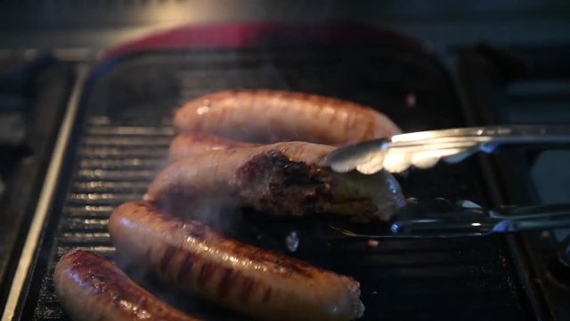 Sausages cooking on the grill, being turned using a set of tongs.