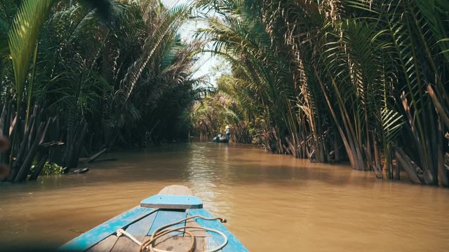 Camera tracks over the shoulder of a young millennial woman sitting on a small boat while sailing along a river in the jungle