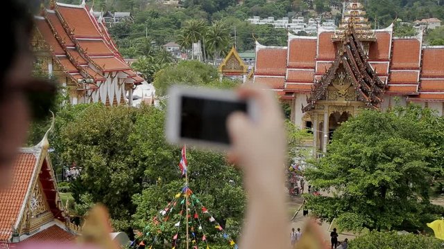 Close up of brunette female tourist, who is taking photos on the smartphone on view point in Tailand. Woman with brand-new device in her hand is making pictures of beautiful buddhist temples with red