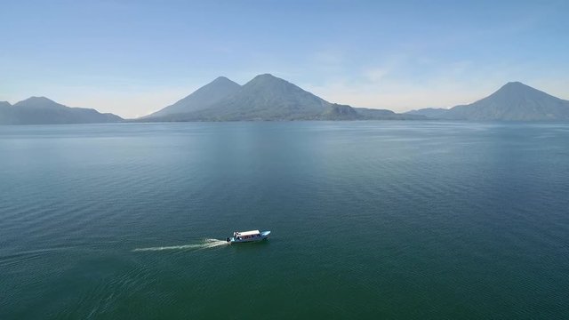 Aerial over a boat on Lake Amatitlan in Guatemala reveals the Pacaya Volcano in the distance.