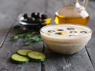 Freshly made tzatziki in a glass bowl with garlic and oil on a dark wooden table.