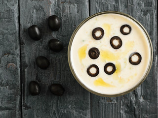 Freshly made tzatziki in a glass bowl with olives on a dark wooden table.