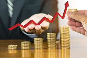 Businessman hand holding red arrow up over money coin stack arranged as a graph with man hand holding pile of coin, concept of money growth and save money