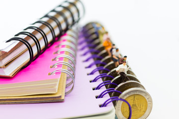 Miniature people: businessman sitting on coins reading newspaper on a big book. Image use for background education or business concept.