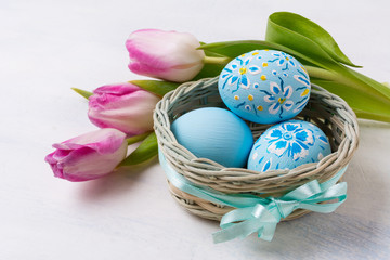 Easter blue painted eggs in thebasket and pink tulips