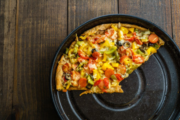 Slices of pizza on metal tray on dark table, from above and blank space.