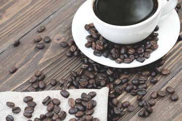 Black coffee in white cup surrounded by roast coffee bean.