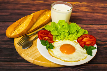 Breakfast with bread, fried eggs, milk and vegetables and fried tomato pieces on wood background