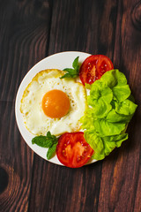 Breakfast with fried eggs and vegetables and fried tomato pieces on wood background
