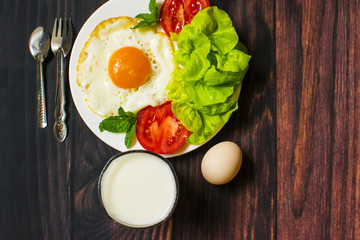 Breakfast with bread, fried eggs, milk and vegetables and fried tomato pieces on wood background