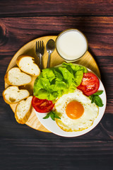 Fototapeta na wymiar Breakfast with bread, fried eggs, milk and vegetables and fried tomato pieces on wood background