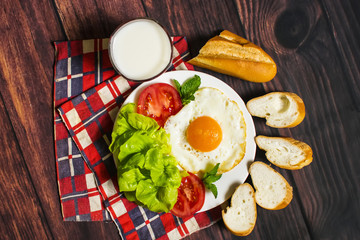 Breakfast with bread, fried eggs, milk and vegetables and fried tomato pieces on wood background
