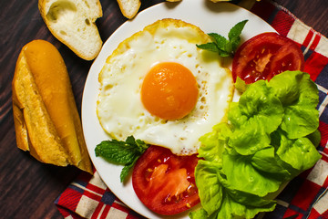 Breakfast with bread, fried eggs, milk and vegetables and fried tomato pieces on wood background