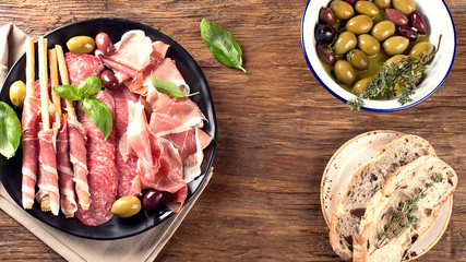 Plate with prosciutto, salami, bread sticks and olives.