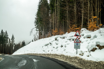 Winter trip by car through the mountain pass. A sharp turn and warning road signs on the road in the mountains