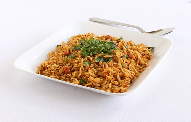 Puliyogare, south Indian traditional and popular vegetarian rice dish, in a plate, and in the background is a steel spoon.