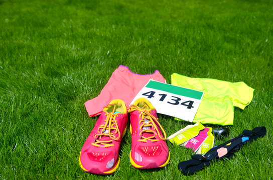 Running shoes, marathon race bib (number), runner gear and energy gels on grass background, sport competition, fitness and healthy lifestyle concept
