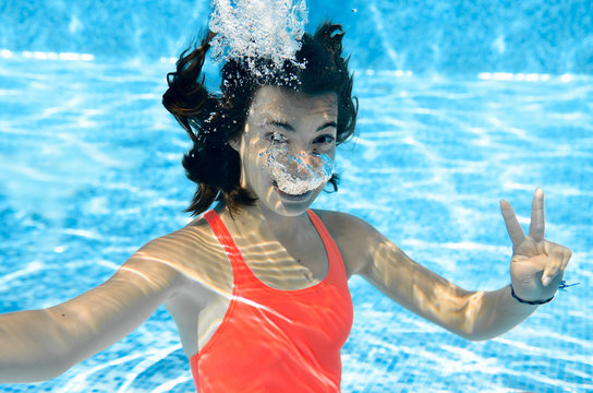 Child swims in swimming pool underwater, happy active teenager girl dives and has fun under water, kid fitness and sport on family vacation on resort
