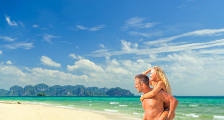 Happy man in love giving piggyback ride to smiling woman at the beach. Couple enjoying vacation at...