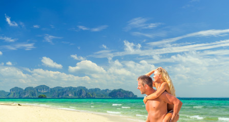 Happy man in love giving piggyback ride to smiling woman at the beach. Couple enjoying vacation at beach