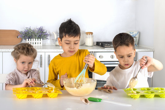 The little girl and two boys cook cake in kitchen of the house.