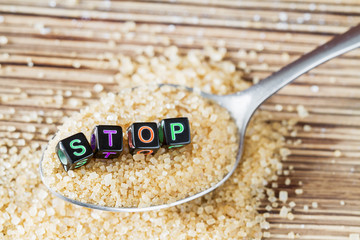 Brown sugar in metal spoon on the brown wooden background with the inscription STOP from small...