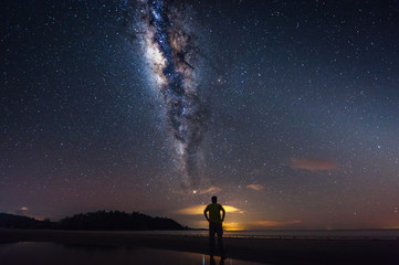 Rear view of man and Milky Way Galaxy at the beach. Image contain soft focus, blur and noise as night photo required long expose and high ISO.