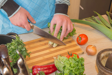 Male hands cutting vegetables on kitchen blackboard. Healthy food. Man preparing vegetables, cooking healthy meal in the kitchen