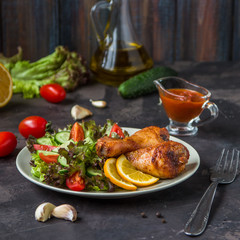 Fried chicken legs and fresh salad on a dark background