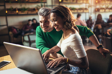 Young interracial lovers spending time in cafe watching media together on laptop.