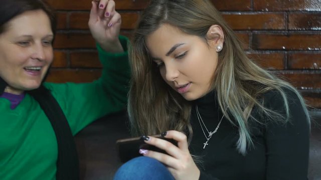 Mom is on friendly terms with the daughter of a teenage return. Together they look at something on the phone.