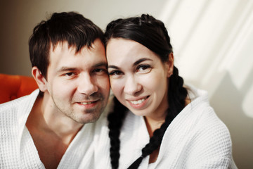 Young husband and wife of white coats play and smile in an orange armchair in a hotel room. Close up.