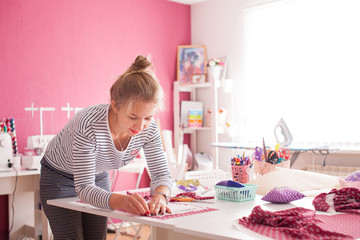 young woman seamstress making pattern on fabric with tailors chalk. Girl working with a sewing pattern. Hobby sewing as a small business concept. Tailor measuring textile material