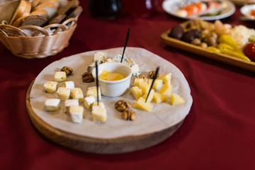 Honey in a white small bowl in focus on a cheese plate. Cheese plate served with nuts and honey. Food