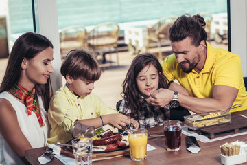 Father and mother with children enjoying meal in restaurant.
