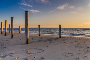 The light of golden hour at the beach with wooden piles and hearts drawings in the sand Petten, Holland, North Sea