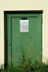 Old green steel door with hazard notes on plates