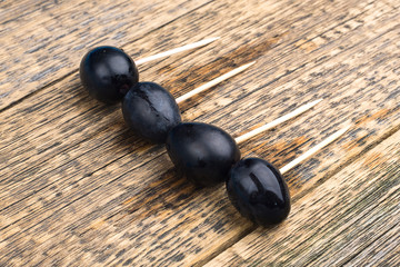 four dark berries are planted on wooden toothpicks, on a wooden background are traces of water