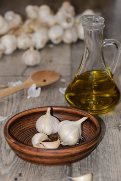 Garlic in a clay dish with a wooden spoon and olive oil on a table