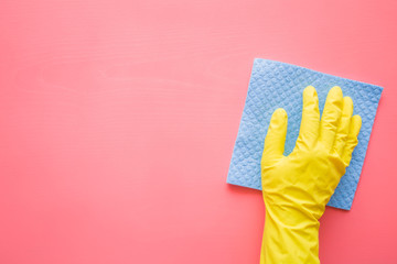 Employee hand in rubber protective glove with sponge cloth wiping pink table, wall or floor surface in room, bathroom, kitchen. Early spring or regular cleanup. Commercial cleaning company concept.
