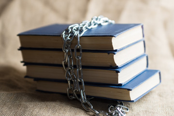 burlap on which lie forbidden books bound by a chain of metal, a stack of books