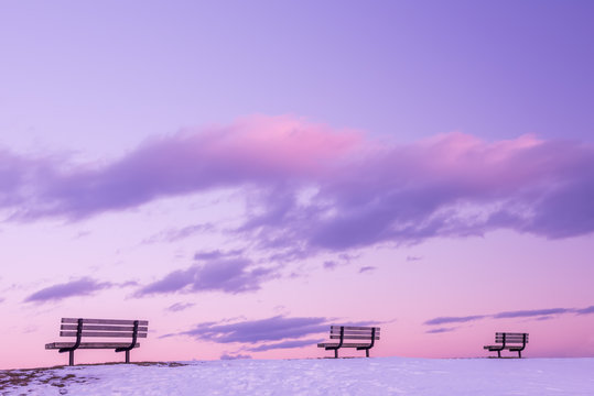 A series of benches against the background of a gentle pink sky with clouds. Minimalism.
